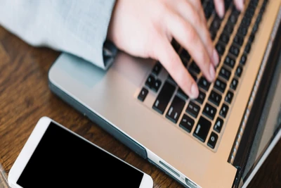 Person tippt am Laptop neben Smartphone – Symbol für digitale Kommunikation zwischen Hausverwalter und Eigentümer