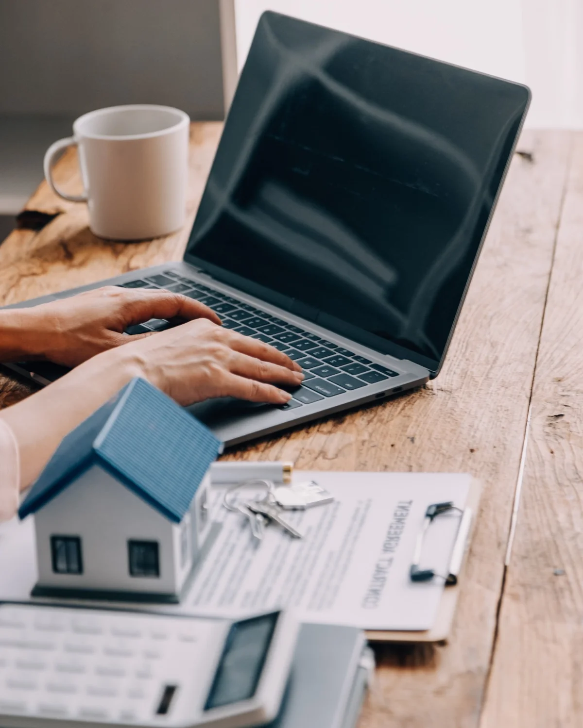 Hausverwaltung am Laptop mit Unterlagen, Modellhaus und Schlüsseln – professionelle Immobilienverwaltung durch RGI Immobilien in Pfronten, Füssen und Kempten